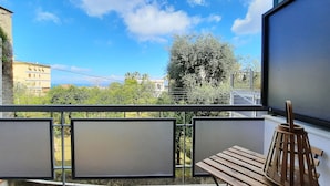 A balcony with a wooden table and chairs, a TV, and a view of greenery and buildings.