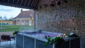 Een buitengebied met stenen muren, een jacuzzi, stoelen en een uitzicht op een gebouw op de achtergrond.