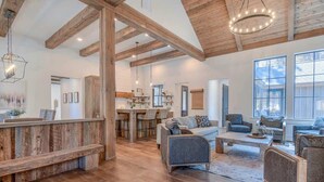 A spacious living area with wooden floors, a high ceiling with exposed beams, and a large window providing natural light. - Guest Fav! Pool table, ping pong, foosball, paddle boards, AC, Hot tub, pet friendly, luxury home, family friendly, this home has it all! (Sunriver)