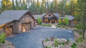 A rustic cabin-style home with a large garage, a covered porch, and a driveway leading to the entrance. - Guest Fav! Pool table, ping pong, foosball, paddle boards, AC, Hot tub, pet friendly, luxury home, family friendly, this home has it all! (Sunriver)