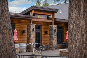 A wooden building with a sign reading "Village Grill." There are stone pillars, a bicycle, and barrels outside. - Guest Fav! Pool table, ping pong, foosball, paddle boards, AC, Hot tub, pet friendly, luxury home, family friendly, this home has it all! (Sunriver)