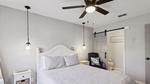 Un dormitorio con una cama blanca, ventilador de techo y mesita de noche con lámpara.