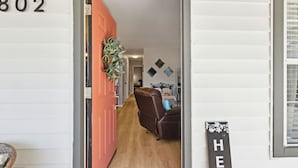 Un pasillo con una puerta roja, un sillón de cuero marrón y un letrero de bienvenida.