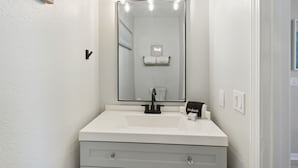 Un baño con un lavabo blanco, un grifo negro y un espejo con luces sobre él.