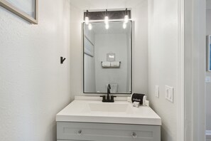 A bathroom with a white sink, a black faucet, and a mirror with light fixtures above it.