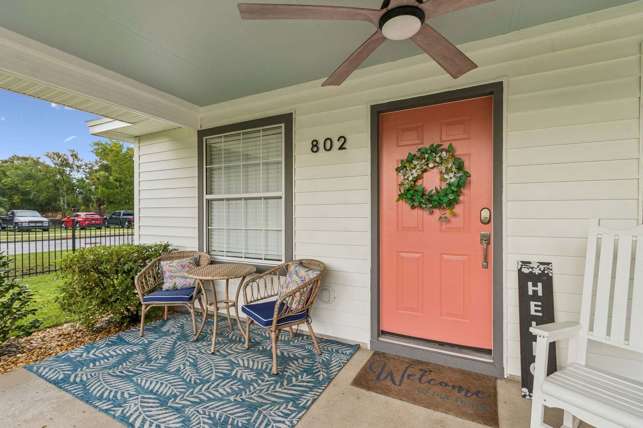 A house with a number 802 on the door, a porch with wicker chairs, a blue patterned rug, and a welcome mat.