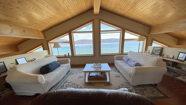 Un salon chaleureux avec deux canapés blancs, une table basse et une grande fenêtre donnant sur un paysage magnifique.