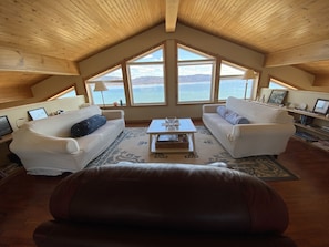 A cozy living room with two white sofas, a coffee table, and a large window overlooking a scenic view. - Cabot trail, walk to beach, luxurious living space, gorgeous Atlantic Ocean view (Chéticamp)