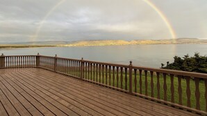 Une terrasse en bois dotée d’une balustrade, d’où l’on peut admirer un lac et des collines au loin.