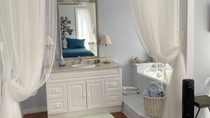 Une chambre à coucher avec un lit, une coiffeuse avec un miroir, un lavabo et une fenêtre ornée de rideaux légers.