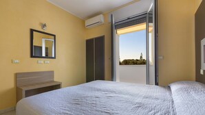 A bedroom with a bed, a bedside table, a wardrobe, a mirror, and an air conditioning unit. - Residence Solaris - Bilo PP Fronte Mare (Torre Specchia Ruggeri)