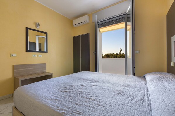 A bedroom with a bed, a bedside table, a wardrobe, a mirror, and an air conditioning unit.