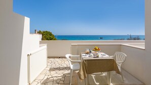 Un balcón con una mesa dispuesta para dos personas, con vista a un mar azul y despejado.