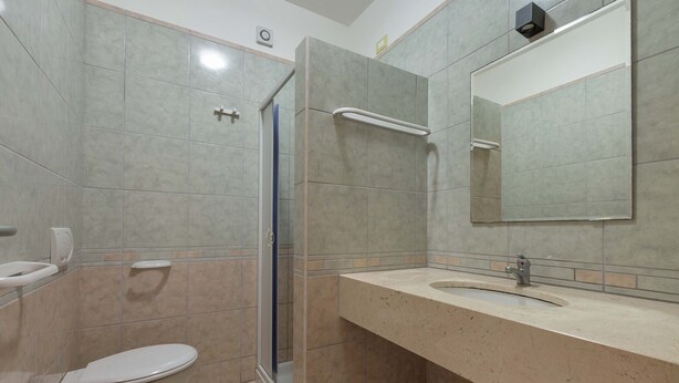 A bathroom with a toilet, bidet, sink, mirror, and shower.