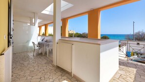 A modern kitchen with a dining area, large windows with ocean views, and a stone-tiled floor.