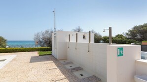 Zona de baños portátiles con suelo de baldosas y vistas al mar.