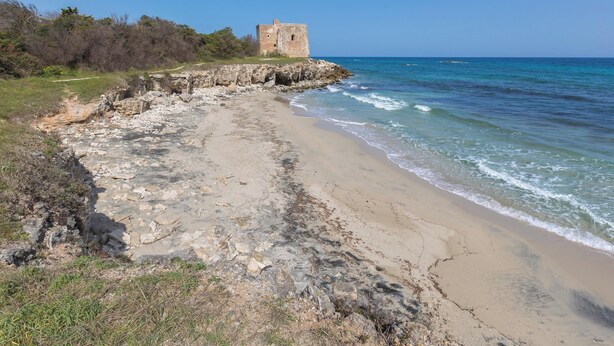 Un paisaje costero con una playa rocosa, una pequeña construcción de piedra y el océano.