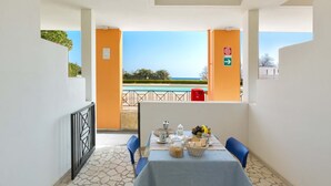 Un balcón con mesa lista para el desayuno, vista a la piscina y un extintor de incendios rojo.