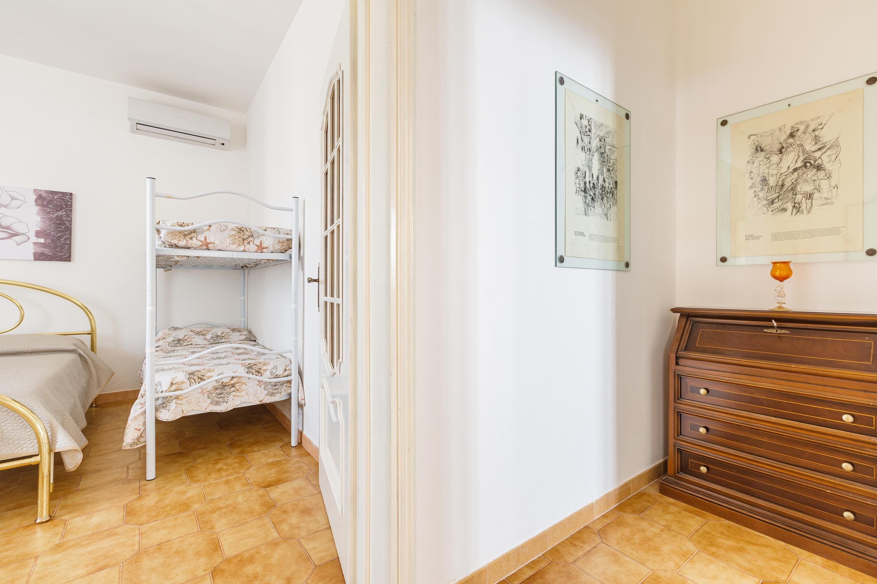 Een kamer met een stapelbed, een houten dressoir en twee ingelijste kunstwerken aan de muur.