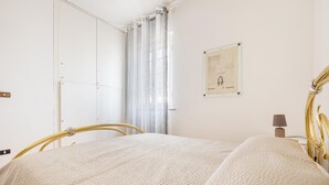 Makuuhuoneessa on sänky, yöpöytä, lamppu, seinällä oleva kehystetty kuva ja ikkuna, jossa on verhot.