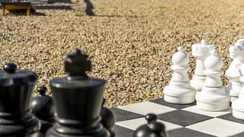 A chessboard with black and white pieces, a gravel surface, and a fence in the background.