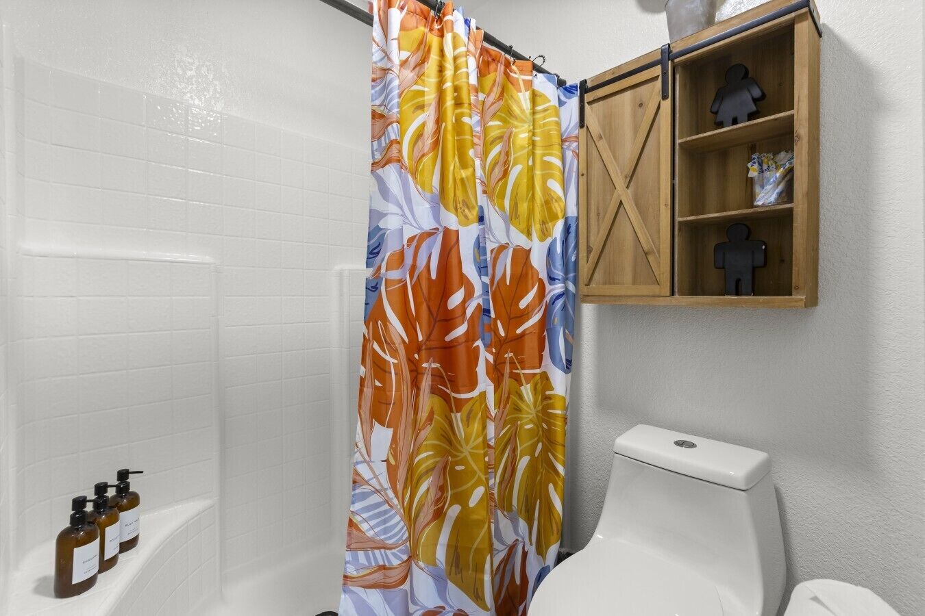 A bathroom with a shower curtain, toilet, and a wooden shelf with toiletries.