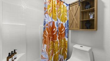 A bathroom with a shower curtain, toilet, and a wooden shelf with toiletries.