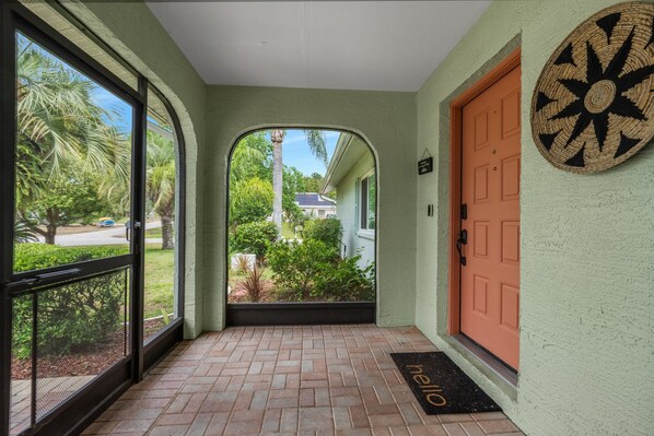 A covered porch with a door, a welcome mat, and a view of a residential area.