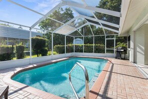 A covered swimming pool with a metal ladder, surrounded by a brick patio and a white fence.