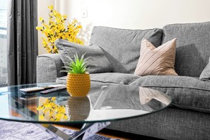 Una sala de estar moderna con un sofá gris, una mesita de centro de vidrio y una planta pequeña.
