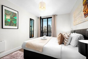 A modern hotel room with a large bed, a view of the city, and a framed abstract painting.