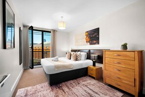 A modern bedroom with a bed, bedside tables, a dresser, and a cityscape painting.