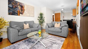 Un salon moderne avec deux canapés gris, une table basse en verre et un tableau représentant un paysage urbain accroché au mur.