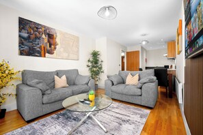 Ein modernes Wohnzimmer mit zwei grauen Sofas, einem Glastisch und einem Stadtbild an der Wand.