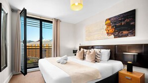 Une chambre d’hôtel avec un lit, une table de chevet, une lampe, un tableau et une vue sur le paysage urbain, visible à travers une grande fenêtre.