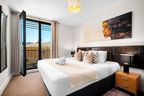 Ein Hotelzimmer mit Bett, Nachttisch, Lampe, einem Gemälde und Blick auf eine Stadtlandschaft durch ein großes Fenster.
