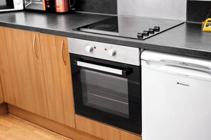 Una cocina con horno integrado y lavavajillas, armarios de madera y encimera negra.