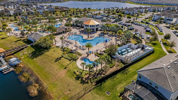 A residential area with a large swimming pool, multiple houses, and a lake in the background.