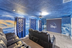 Un cine en casa con un mural de estrellas, una pantalla de proyector y sillones de cuero reclinables.