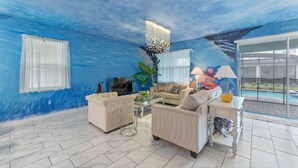 A room with a blue mural, a sofa, a coffee table, a TV, and a lamp.