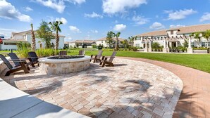 A patio area with a fire pit, lounge chairs, and a brick pathway leading to a residential complex.