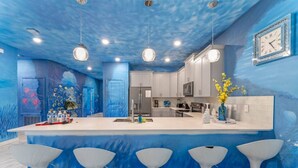 A kitchen with a central island, bar stools, a clock, and a wall mural.