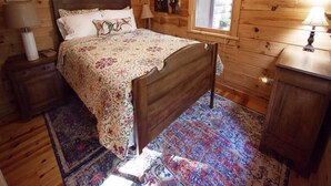 Un dormitori d'una cabana de fusta amb un llit, tauletes de nit, una finestra i una catifa.