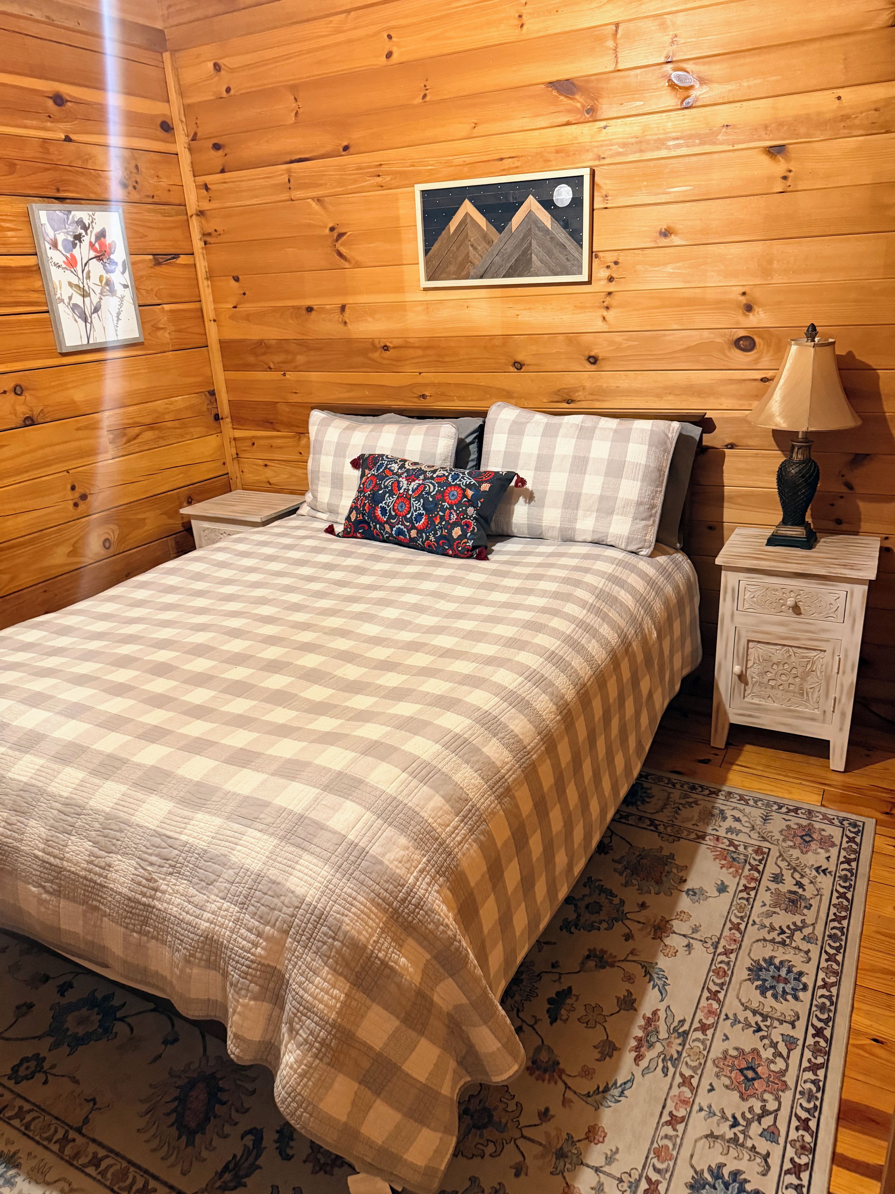 A wooden-paneled room with a bed, a nightstand, a lamp, and a framed picture on the wall.