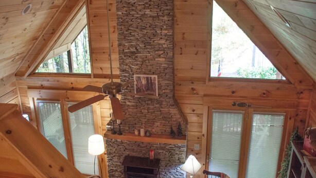 Interior d'una cabana amb una llar de pedra, bigues de fusta i un sostre alt.