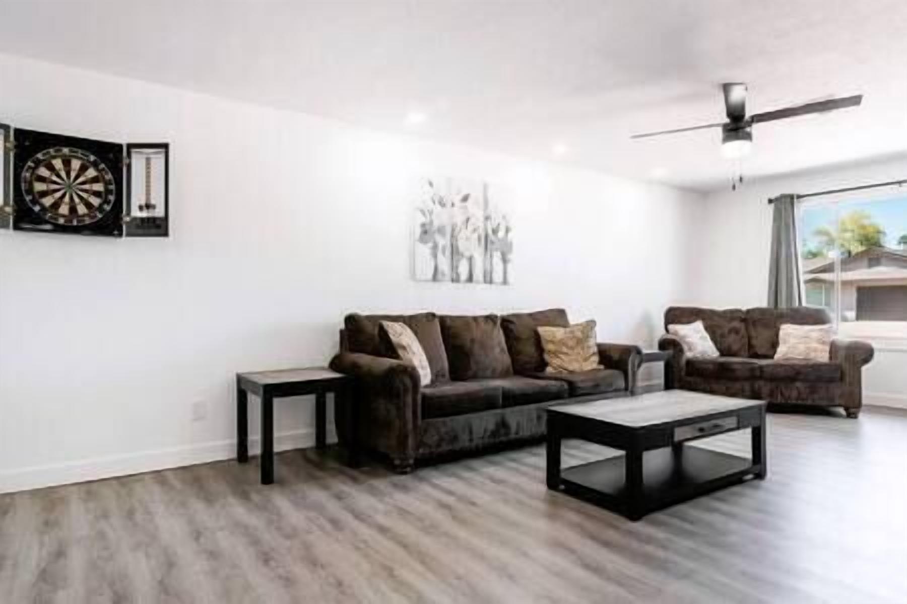 A modern living room with a dark brown sofa set, a coffee table, and a dartboard on the wall.