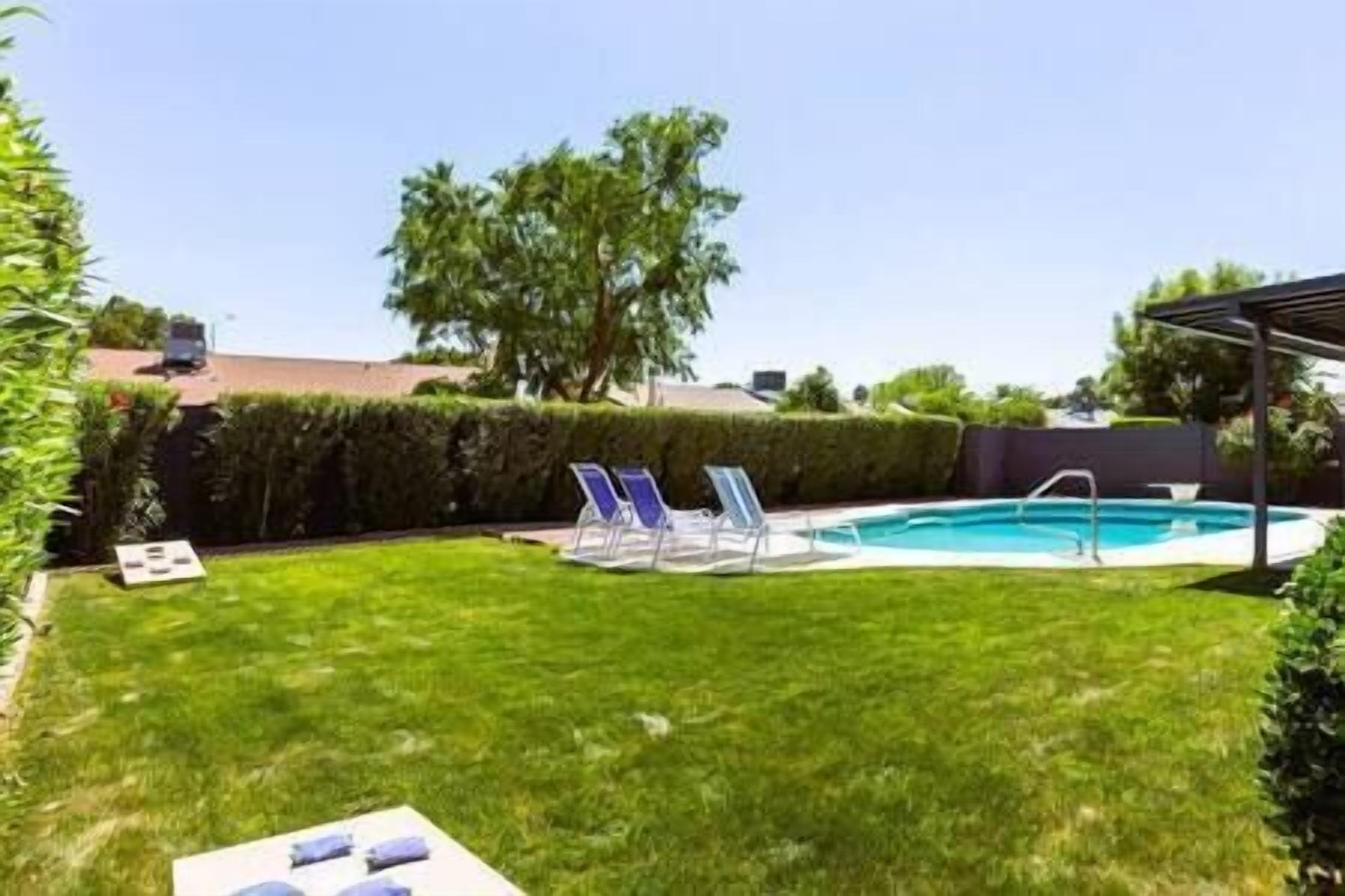 A backyard with a swimming pool, a lawn, and a pergola.