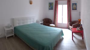 A bedroom with a bed, a nightstand, a chair, a small table, and a door with curtains. - Apartment with terrace overlooking the lake, a stone's throw from the port (Mèze)