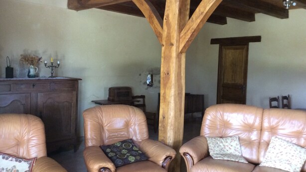 Um interior rústico com vigas de madeira, poltronas de couro, um armário de madeira e uma pequena mesa com objetos decorativos.