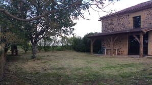 Um edifício rústico de pedra com um alpendre coberto e um gramado.
